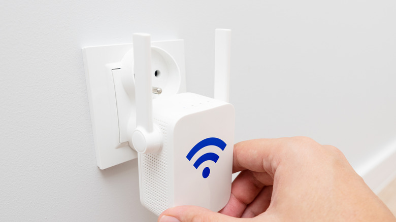 An image of a hand plugging a Wi-Fi extender into a socket