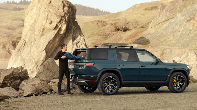 Man unloading a surfboard from a Rivian R2