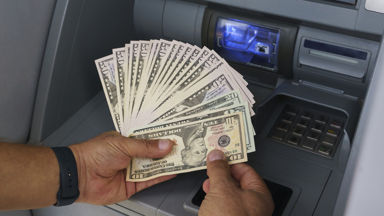 Close up of hands holding dollar bills in front of an ATM