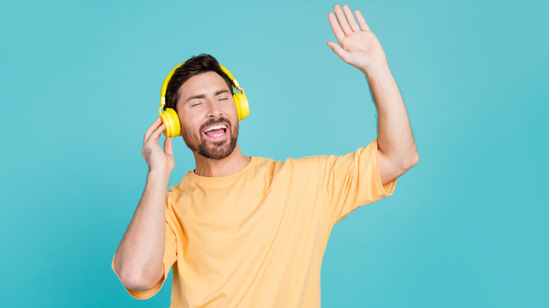 Happy guy jamming to music with one arm in the air and the other arm resting on his bright yellow headphones