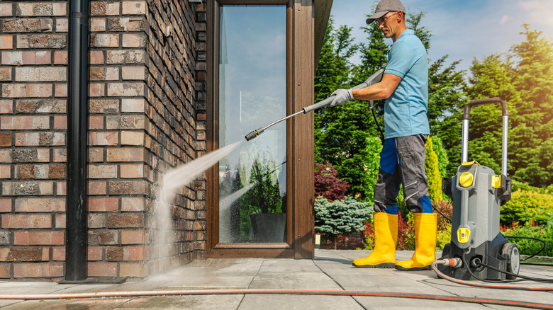 A man wearing yellow boots cleaning his property's brick wall with a pressure washer