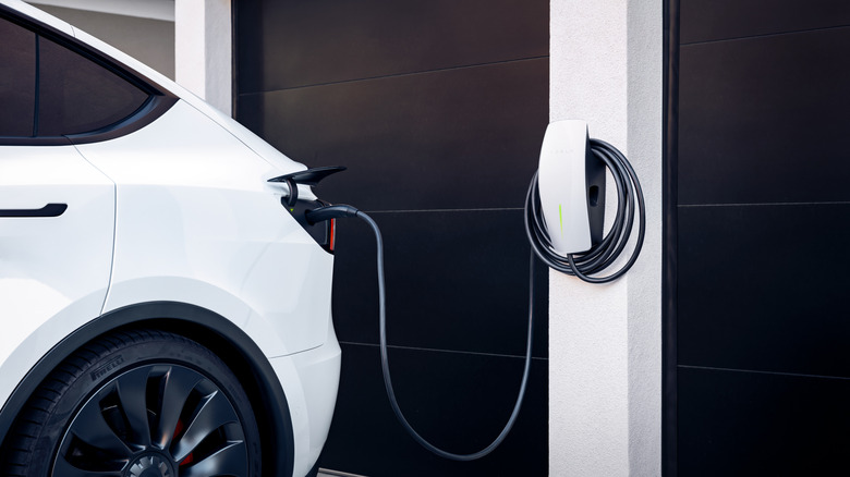 A white Tesla electric car charging at a home wall-mounted charger.