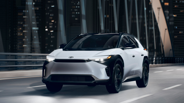 A white and black Toyota bZ4X electric SUV driving across a city bridge at night.