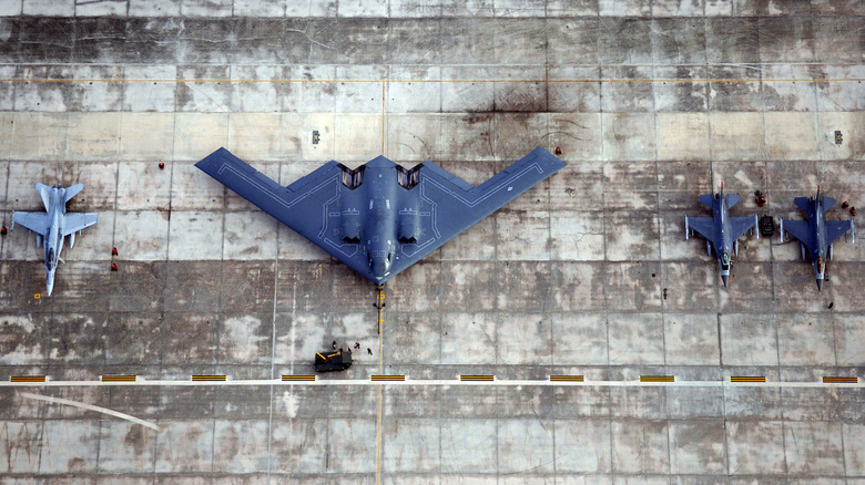 Overhead view of a B-2 Spirit bomber on the runway with fighter jets either side