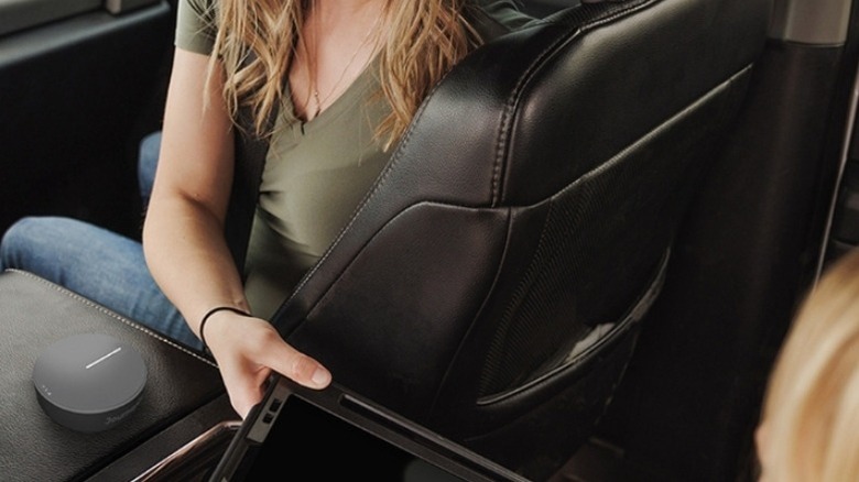 Woman passing a tablet to a child in the backseat of a car