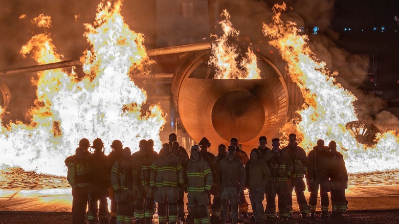 Military firefighters watch an aircraft engulfed in flames during training