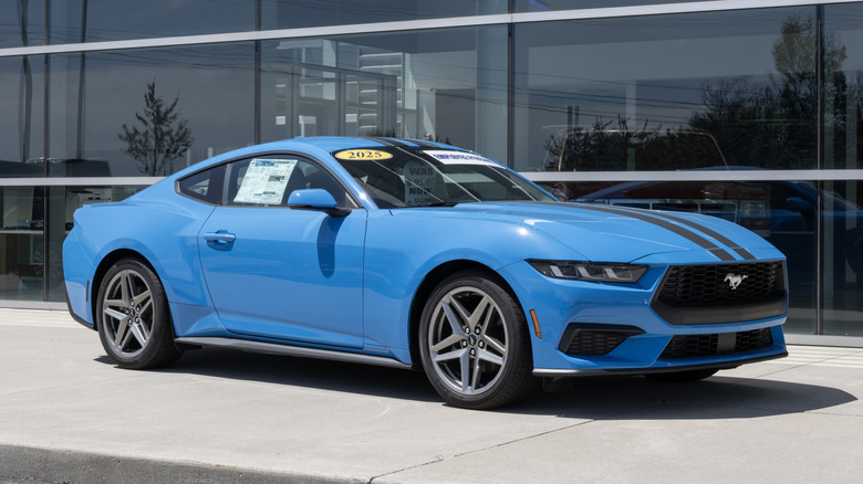 A blue EcoBoost four-cylinder base 2025 Ford Mustang parked in front of a dealership.
