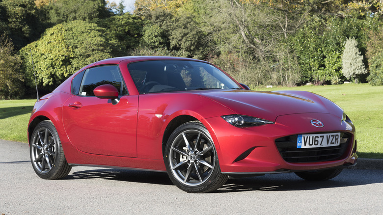 A red Mazda MX-5 Coupe parked on a sunny day in front of a grass field.