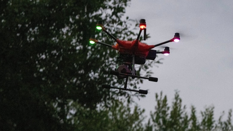 A drone in flight against a tree-lined backdrop.
