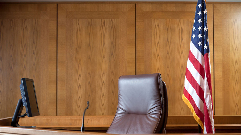 A courtroom with a computer monitor, a brown leather chair, and the American flag