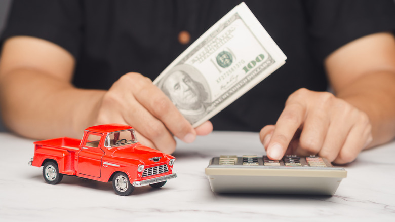A person holding money and using a calculator at a table with a small red model truck.