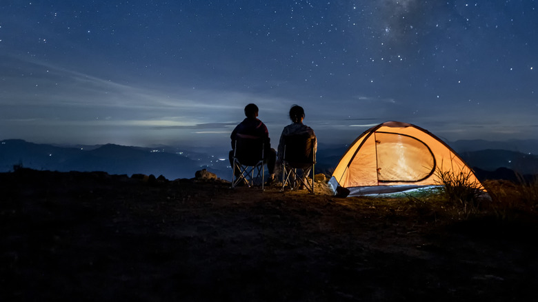 Two people camping with a well lit tent