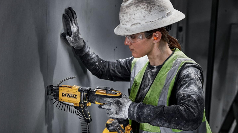 Woman in white hardhat using DeWalt nail gun to hang drywall