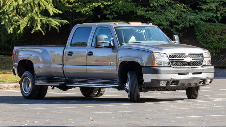 Silver Chevy Silverado dually in parking lot with trees behind