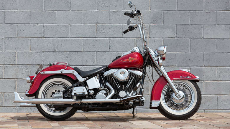 A Harley-Davidson Heritage Softail motorcycle, parked along a grey clay brick wall, facing right, side view visible