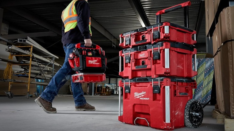 Three Milwaukee toolbox stacked together and a man carrying a tool bag in hand
