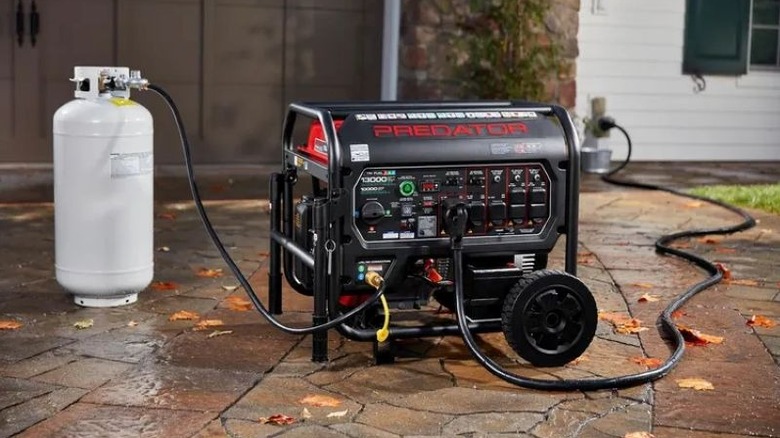 A portable generator on a driveway outside a home, hooked up to a propane tank