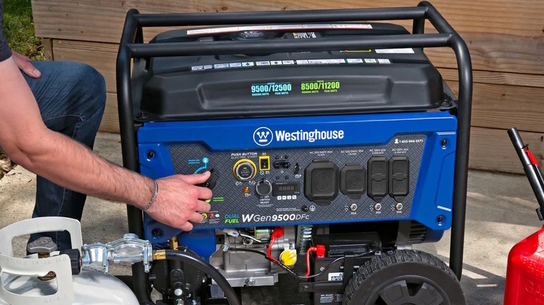 Person turning on a portable generator with gasoline and propane tanks nearby