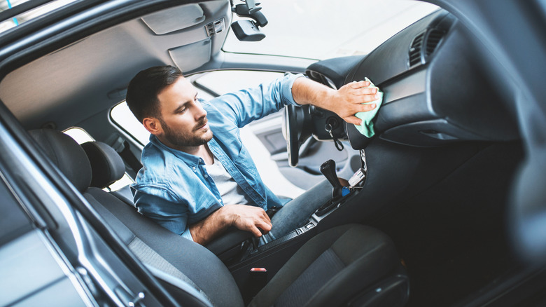 man cleaning dashboard of car