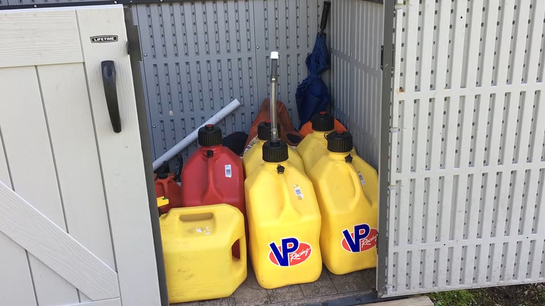 A number of yellow and red gas containers, also called jerry cans, in an outdoor storage unit, ostensibly for long term use.