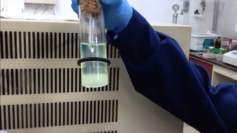 A lab technician in latex gloves demonstrating a pour point test for fuel under ASTM D97 standards.