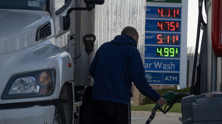 A man buying diesel fuel for his truck with a digital price board showing the prices in the back in early 2026.
