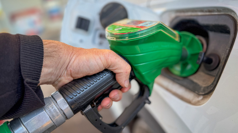 A man filling diesel into his silver car at a petrol station forecourt in the middle of the day.
