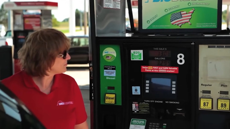A woman in a red polo T-shirt standing in front of a B20 biodiesel pump at a gas station in America.