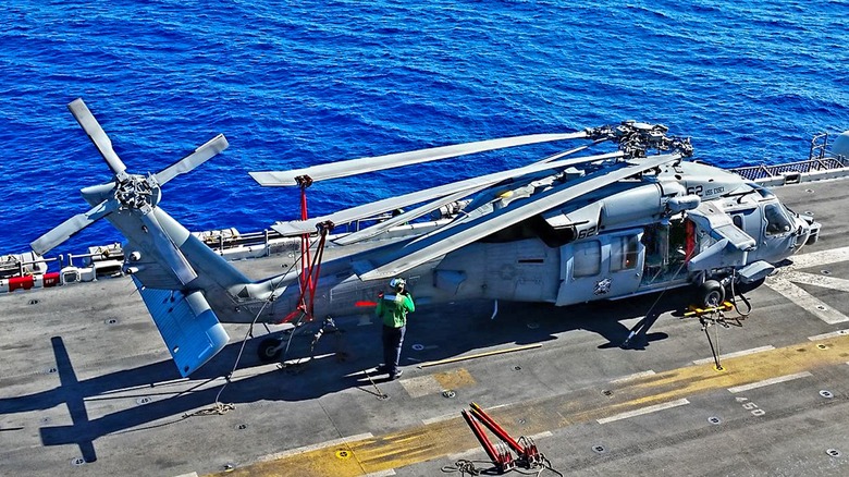 An MH-60 with its rotors folded back aboard an aircraft carrier