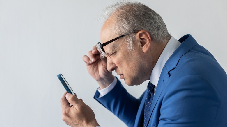 Squinting at smartphone with glasses raised