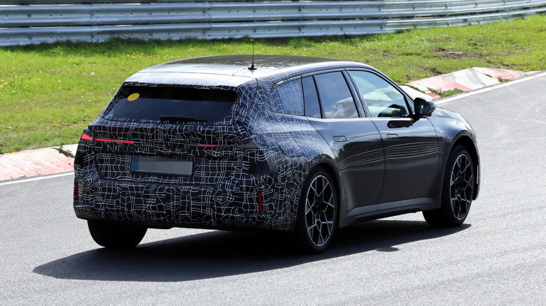A rear three-quarter view of a black camouflaged BMW i3 Touring driving on a track.