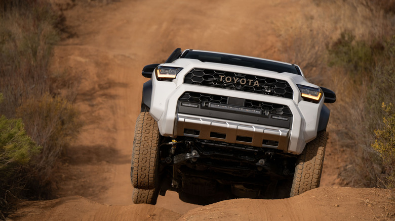 Front view of white Toyota 4Runner lifting tire on off-road trail.