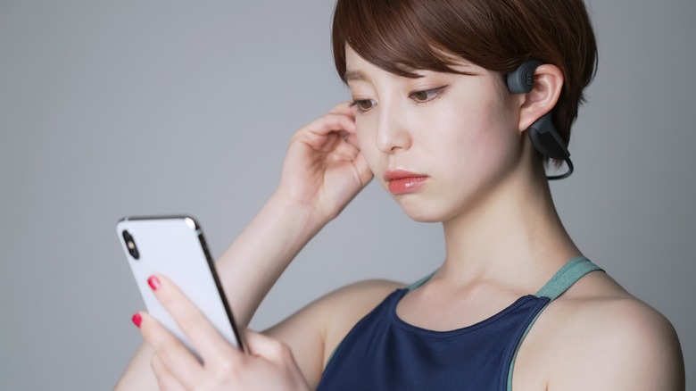 woman adjusting bone conduction headphones while looking at phone