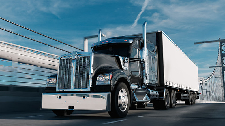 Typical American big-rig truck hauling white cargo container across bridge, front-left view