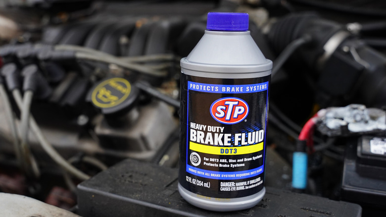 Container of brake fluid with car engine in background