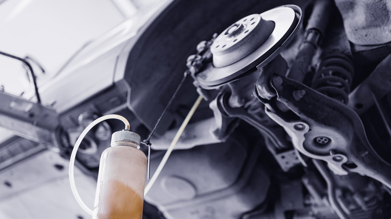 An off-screen mechanic flushing out the brake fluid from a car's brakes