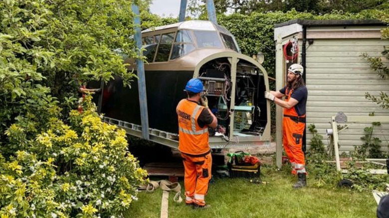 Two men moving the replica Lancaster cockpit out of Léon Ellison's yard