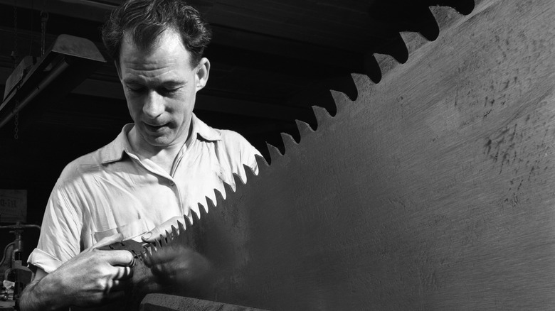 Black and white photo of a man holding a sharp saw in his hand
