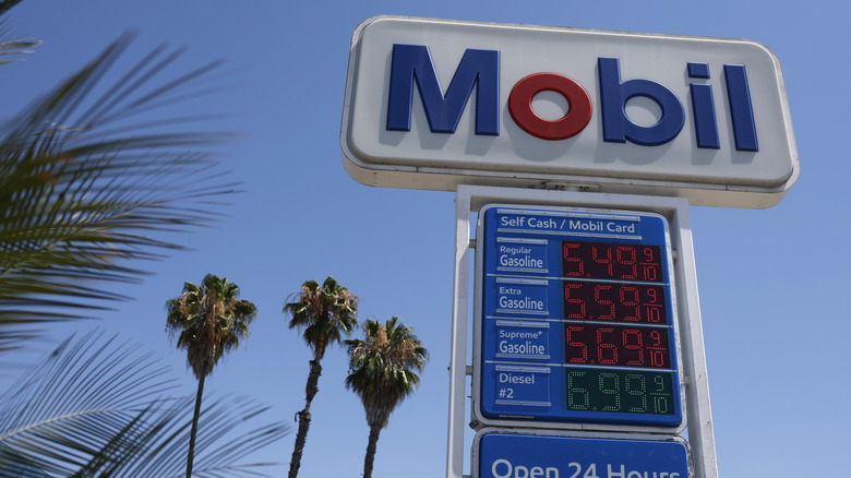 A California Mobil gas station sign showing gas prices with palm trees in the distance.