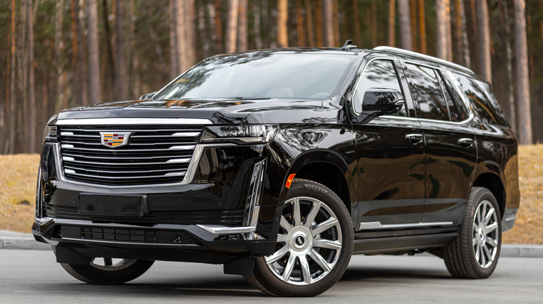 A black Cadillac Escalade parked in front of trees.