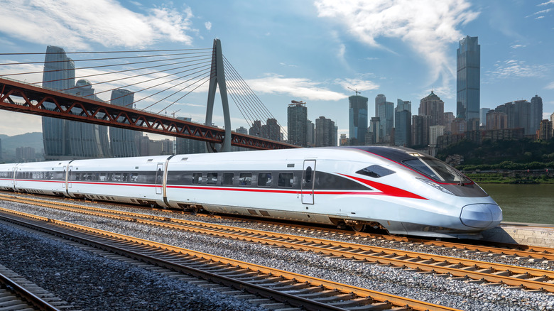 A silver and red high-speed train on track with a cityscape behind it