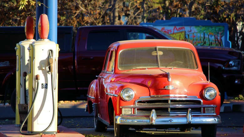 Red 1950 Plymouth Deluxe at vintage gas station with Ram truck in background