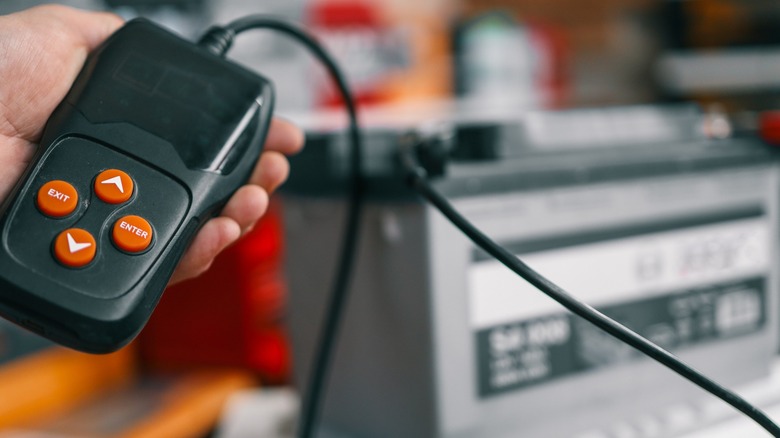Battery-tester in hand with a car battery in the background