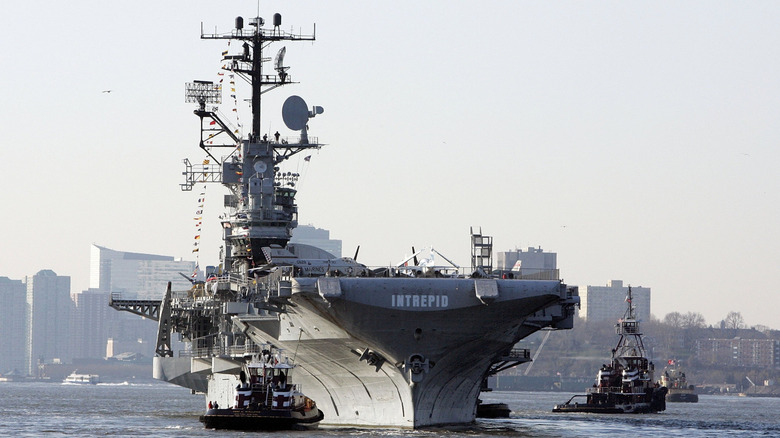 Aircraft carrier being maneuvered by tugs