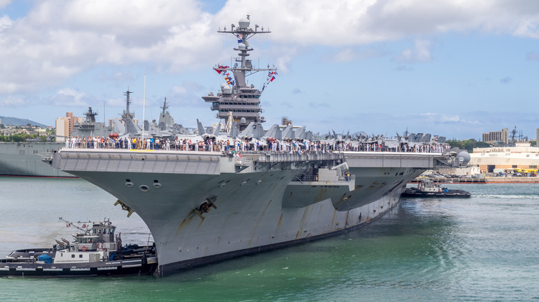 Aircraft carrier with tugs pushing from the bow and stern
