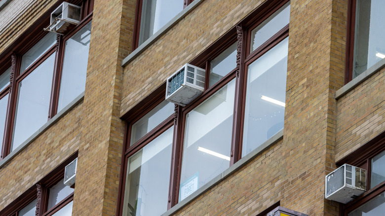 Window air conditioner units installed in windows of apartment building.