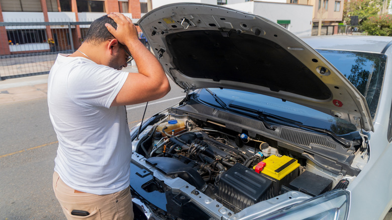A man standing over his car's engine with his hands on his head in confusion