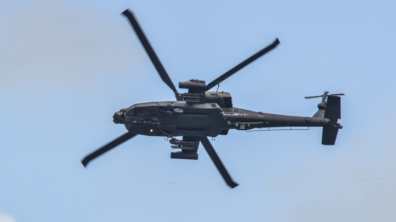 An AH-64 Apache helicopter rotating in the air, viewed from below