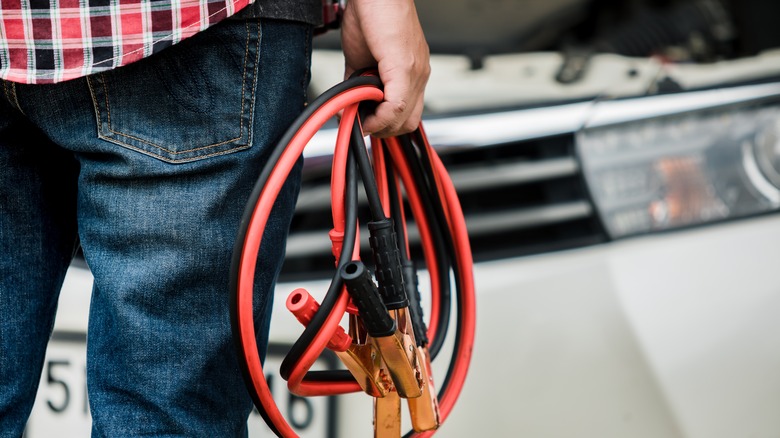 Man holding jumpier cables in front of a car