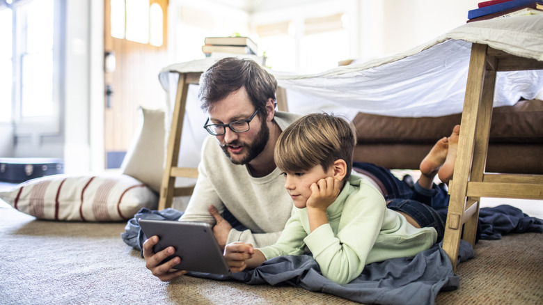 Father and son watching digital tablet in homemade fort.